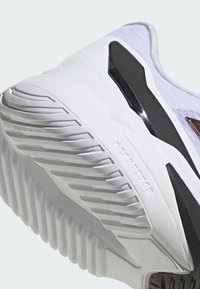 Biała podeszwa sportowego buta z teksturowanej gumy, kanciastym wzorem, czarnymi akcentami i podniesionymi wzorami na bieżniku dla lepszej przyczepności.