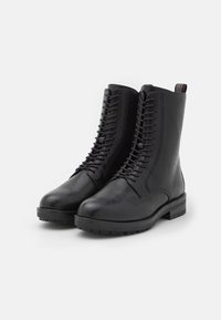 Botas de combate negras de cuero con cordones, suela gruesa y tiradores en la parte trasera, mostradas sobre un fondo blanco liso.