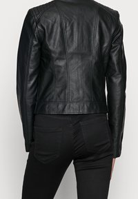 Giacca da moto in pelle nera con accenti imbottiti sulle spalle, design aderente e texture liscia. Abbinata a jeans in denim neri con tasche posteriori.