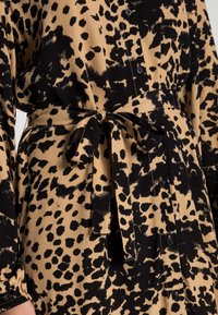 Svart och beige leopardmönstrad klänning med knyt i midjan, lång ärm, knappstängning fram och textilstruktur. Har en avslappnad passform.