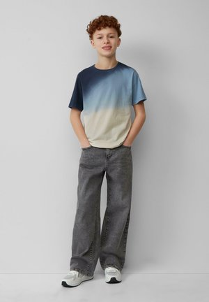 T-shirt à manches courtes avec dégradé allant du bleu foncé au beige clair, associé à un jean gris à jambes larges et des baskets blanches.