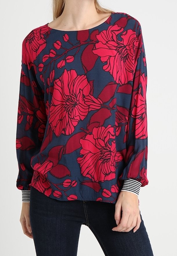 Floral blouse in navy with large red flowers, round neckline, and long sleeves with striped cuffs. Soft fabric, loose fit, and vibrant pattern.