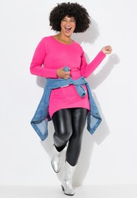 Robe rose à manches longues superposée sur des leggings noirs, surmontée d'une veste en denim nouée ; complétée par des bottes de cowboy argentées brillantes.