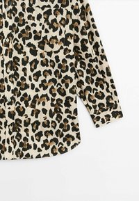 Leopardprint knap-up skjorte i beige med sorte og brune pletter; har en brystlomme og lange ærmer. Blødt stoftekstur.