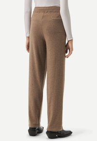 Bruna stickade byxor med en avslappnad passform, utrustade med elastisk midja, bakficka och en slät textur. Bärs med svarta klackskor.