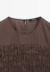 Bruine gestreepte kleding met ronde halslijn, geplooide elastische details onder de borst en een kleine knoopsluiting op de achterkant van de hals.