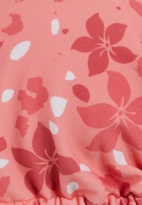 vaaleanpunainen kangas, jossa on kukkakuosi, jossa on suuria punaisia kukkia ja pieniä valkoisia terälehtiä. Koostumus näyttää sileältä ja siinä on ker gather boutonnière.