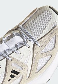 White athletic shoe featuring a mesh upper, suede accents, textured panels, and grey laces. The sole is slightly elevated and rubberized.