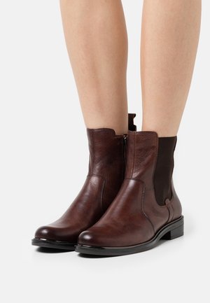 Bottes courtes en cuir marron avec panneaux latéraux élastiques, bout arrondi et petit talon bloc. Texture lisse avec une brillance subtile et des détails de couture.