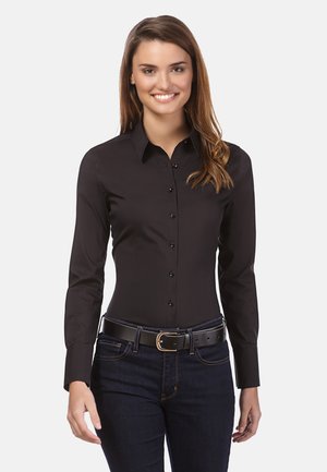 Camicia nera a maniche lunghe con bottoni e colletto, dal design aderente, con bottoni neri; indossata con una cintura nera e jeans scuri.