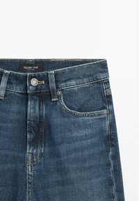 Jeans in denim blu scuro con una texture sottile, dotati di tasche frontali, chiusura con bottone e un'etichetta con la scritta "Massimo Dutti".