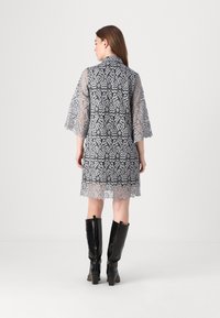 Robe en dentelle noire et argentée avec un motif floral, manches trois-quarts et ourlet festonné, associée à des bottes noires arrivant aux genoux.
