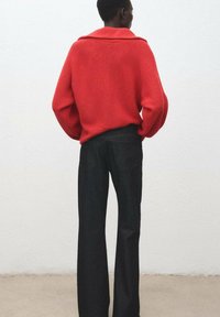 Suéter rojo de punto con cuello ancho, combinado con jeans negros de pierna recta y cintura alta. Se puede apreciar la textura del tejido en el suéter.