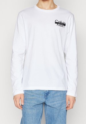 T-shirt blanc à manches longues en coton avec un logo Calvin Klein noir sur la poitrine gauche, encolure ronde et coupe standard.