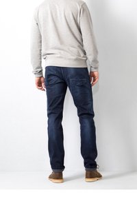 Mörkblå jeans med rak passform, med subtil sömnad på bakfickorna, i kombination med en ljusgrå sweatshirt och bruna skor.