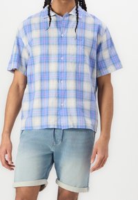 Koszula krótki rękaw w kratę w jasnoniebieskim i białym kolorze z pasteloworóżowymi akcentami. Posiada kieszeń, lekką tkaninę i luźny krój.