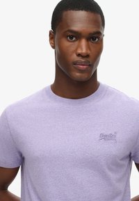 T-shirt girocollo a maniche corte in cotone viola con logo ricamato sul petto. Texture morbida, design aderente.