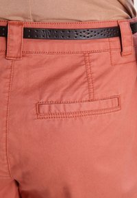 Light coral cotton shorts with a smooth texture, featuring a back pocket and a brown leather belt with perforations.