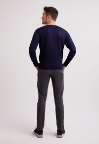 Marinblå stickad tröja med lång ärm, rund halsringning och figursydd design, kombinerad med grå slim-fit byxor och träningsskor.