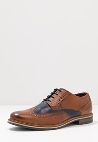 Chaussure en cuir marron avec un panneau en maille noire perforée, design brogue détaillé, bout rond, couture contrastante et semelle empilée.