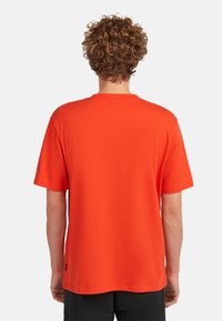 Camiseta de manga corta de color naranja hecha de algodón. Corte relajado con un escote redondo. Textura suave con una etiqueta en la costura lateral izquierda.
