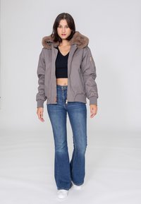 Graue Bomberjacke mit einem braunen Kunstfellkragen, Reißverschlusstaschen und gerippten Manschetten, kombiniert mit blauen, ausgestellten Jeans und weißen Sneakers.