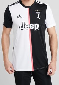 Camiseta de la Juventus en blanco y negro con una franja rosa, que presenta el logo de Adidas, un gran texto de Jeep y tres estrellas doradas encima del emblema del equipo.