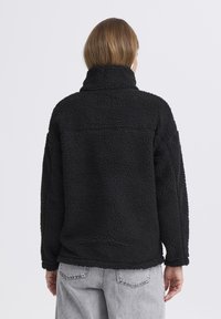 Must have pehmeast fliisist must puller, millel on pehme tekstuur, kõrge krae ja langetatud õlad. Omab vabalt voolavat lõiget ja nähtavaid õmbluse aktsente.