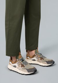 Sneaker aus einer Mischung von beigen, braunen und grauen Materialien, mit einer gesprenkelten weißen Sohle, grauen Schnürsenkeln und einem strukturierten Design.