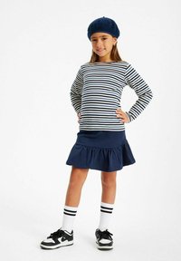 Randig långärmad skjorta i marinblå och krämfärgad, matchad med en marinblå volangkjol. Bärs med svart-vita sneakers och en marinblå basker.