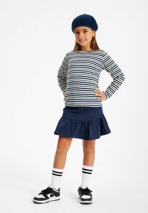 Navy ja cream värviline triibuline pikad varrukad särk, millele on lisatud navy volangiga seelik. Kantud mustade ja valgete adidasetega ning navy bareti ajal.
