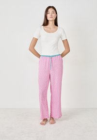 Biała dopasowana koszula z krótkim rękawem w połączeniu z różowymi spodniami piżamowymi z wzorem małych niebieskich kształtów i turkusowym sznurkiem.