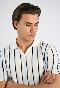 Kortärmad polo t-shirt i vitt med mörkblå och ljusblå vertikala ränder, med V-hals och mjukt, strukturerat tyg.