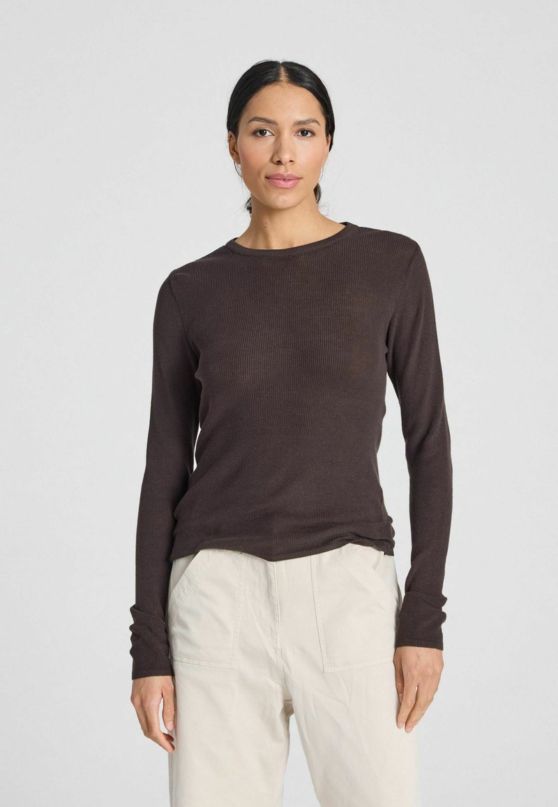 Maglietta marrone a maniche lunghe con scollo rotondo, caratterizzata da una vestibilità rilassata e una texture liscia, abbinata a pantaloni chiari.