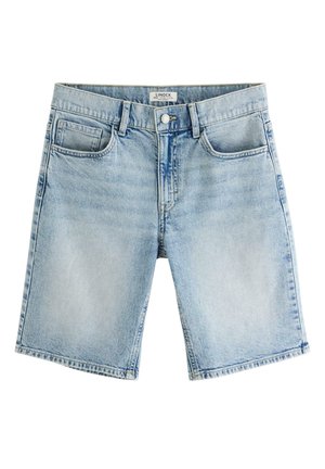 Dreng iført lyseblå polo shirt, knælangt cowboyshorts, hvide høje sokker med striber og hvide sneakers, stående med hænderne i lommerne.