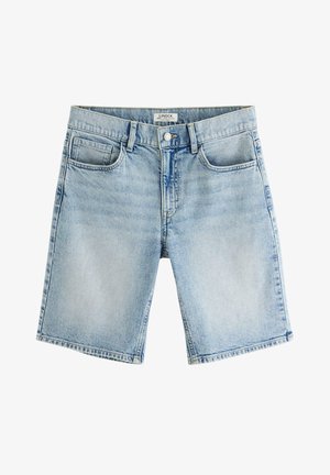 Chłopiec w jasnoniebieskiej koszulce polo, dżinsowych krótkich spodenkach do kolan, białych wysokich skarpetach w paski i białych trampkach, stojący z rękami w kieszeniach.