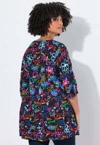 Robe tunique noire à manches courtes avec des motifs de texte colorés et de fleurs, dotée d'une taille froncée et d'une coupe décontractée.