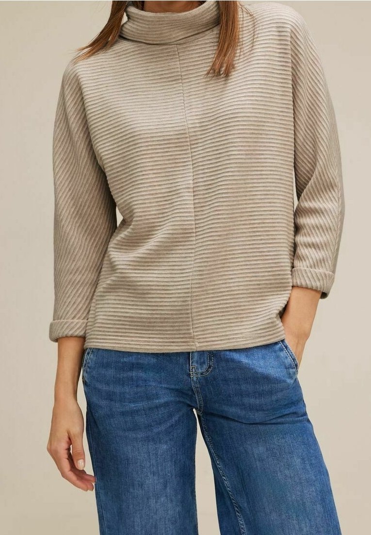 Beige randig tröja med hög krage och trekvartsärmar. Tyget verkar mjukt och matchas med blå vida jeans.