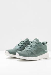 Grüne Netz-Sportschuhe mit weißer Außensohle, strukturiertem Obermaterial, schnürbarem Vorderteil und Logo-Akzent. Für Komfort und Flexibilität entworfen.