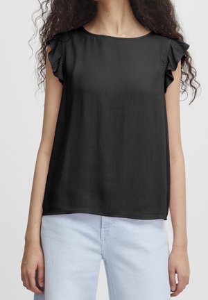 Czarna bluzka bez rękawów z falbaniastymi krótkimi rękawkami noszona z jasnoniebieskimi dżinsami na osobie o kręconych włosach.