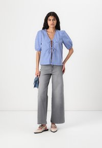 Blå og hvit rutet bluse med knyting foran, puff ermer og v-hals, parret med høyt liv grå vidde jeans og flate sko.