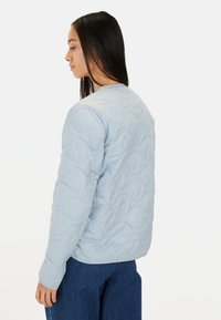Lyseblå quiltet jakke med bølgedesign, stående krave og lange ærmer, lavet af glat stof med en tætsiddende silhuet.