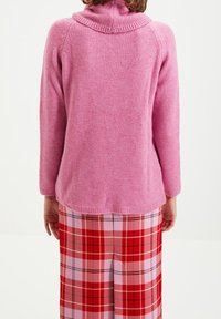 Rosa stickad tröja med hög krage, mjukt material och långa ärmar, ihop med en rosa och röd rutig kjol med vida ben.