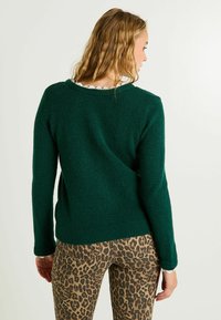 Pull vert foncé en tissu tricoté texturé, avec un col rond et un ourlet côtelé. Associé à un jean skinny à imprimé léopard.