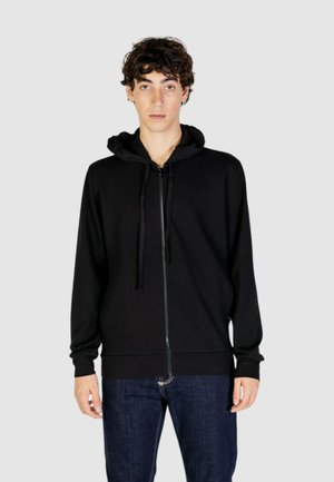 Sort zip-up hoodie i blødt stof med hætte og snor, ribbede manchetter og en glat lynlås. Bæres over mørke denimjeans.