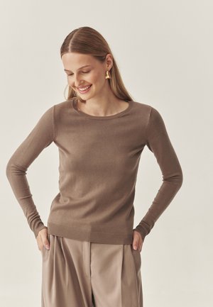 Maglione marrone a maniche lunghe con scollatura rotonda e orlo a coste. La trama morbida si abbina a pantaloni beigi larghi per un look neutro.
