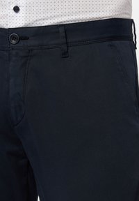 Navy Chino-Hosen mit Knopfverschluss, Gürtelschlaufen und Seitentaschen. Der Stoff hat eine glatte Textur mit einem subtilen Glanz.