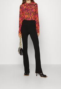 Kleurijke blouse met lange mouwen en zebrapatroon in roze en oranje, gecombineerd met zwarte geribbelde flarebroeken en zwarte sandaaltjes met hakken.