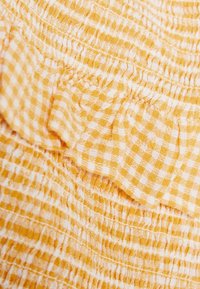 Žlutá a bílá kostičkovaná látka s nabíranou strukturou a volánkovými okraji. Měkký, lehký materiál s alternujícími kostičkovanými vzory.