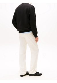 Felpa nera con polsini e orlo a coste, pantaloni bianchi e scarpe nere. La maglietta sovrappone una camicia a righe blu sotto.